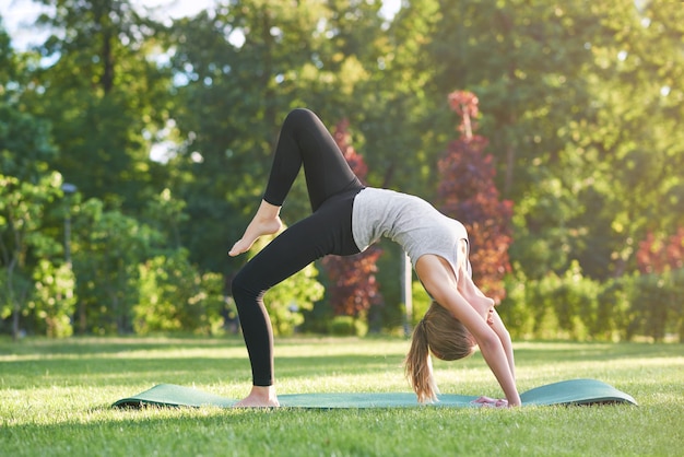 Tir horizontal d'une jeune femme flexible exerçant à l'extérieur dans le parc étirant son dos concept d'acrobatie de gymnastique de mode de vie sportif sain