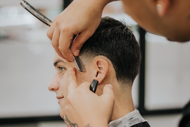 Photo tir latéral d'un gros plan de mains de barbier passant la lame à son client