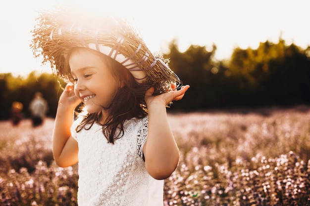 Tir en plein air d'un enfant doux jouant dans un champ de fleurs. Belle petite fille qui court et s'amuse à rire avec une couronne de fleurs sur la tête.