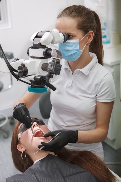 Tir vertical d'un dentiste professionnel à l'aide d'un microscope dentaire, examinant les dents d'une patiente