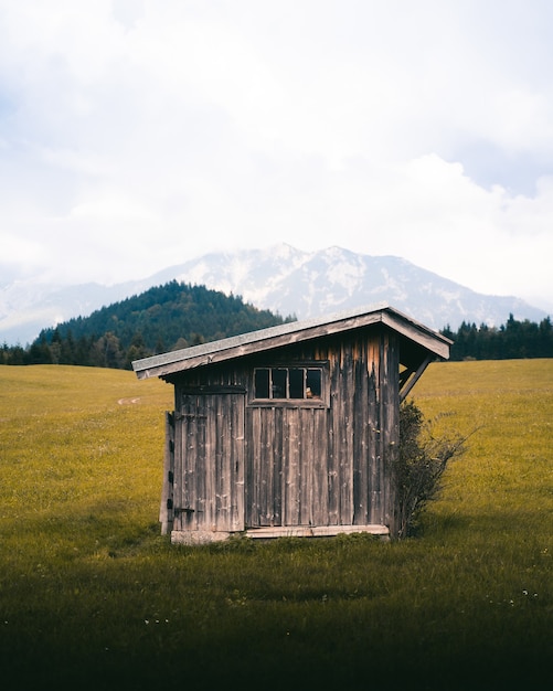 Tir vertical d'une petite maison en bois dans une prairie ouverte avec de hautes montagnes
