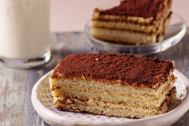 Tiramisu Cake - dessert délicieux sur une assiette, avec un verre de lait sur le fond.