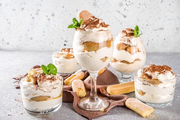 Tiramisu dessert italien traditionnel. Beaucoup de verres avec tiramisu maison avec poudre de cacao chocolat, pierre de pierre grise ou fond de béton.