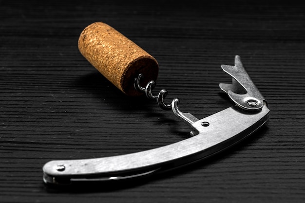 Tire-bouchon sommelier avec un bouchon qui vient d'être retiré de la bouteille de vin, sur bois noir