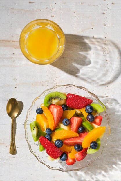 Tiré d'en haut d'un bol transparent rempli de fruits frais sains avec un verre de jus d'orange