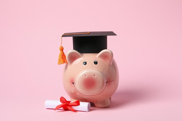 Tirelire avec chapeau de graduation et défilement de degré sur fond rose