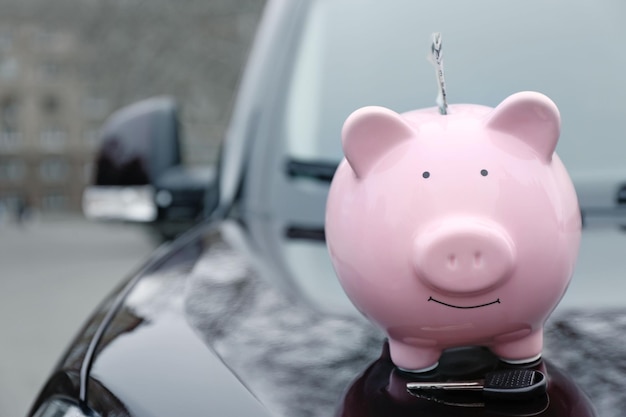 Tirelire cochon avec de l'argent et une clé sur le capot de la voiture dans la rue