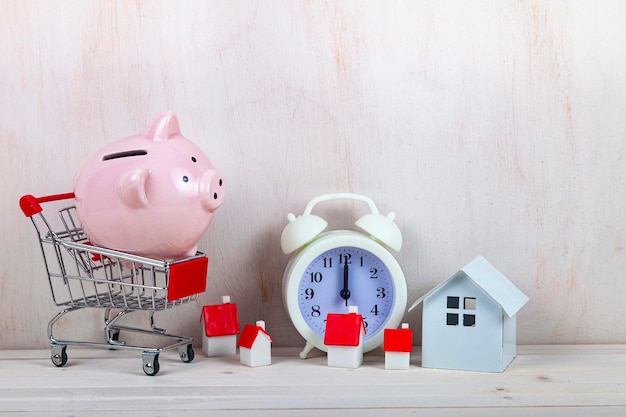 Tirelire cochon, caddie et petites maisons sur le fond de l'horloge. Il est temps d'économiser pour l'immobilier.