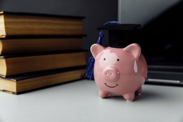 Tirelire rose avec des livres et un chapeau. Collège, diplômé, concept d'éducation.