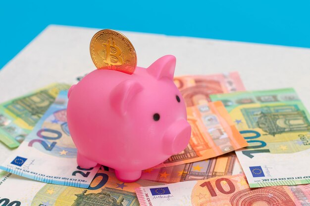 Tirelire rose avec pièce de monnaie bitcoin sur les billets en euros