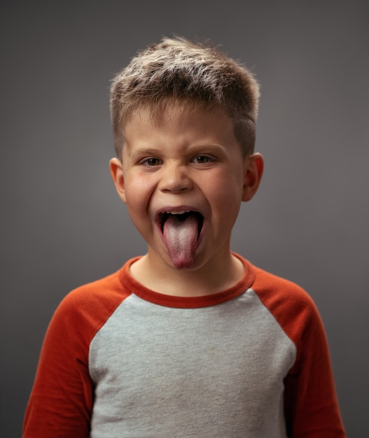 Photo tirer la désobéissance de garçon de langue, mauvais comportement. garçon qui rit drôle en chemise rouge avec les yeux shut