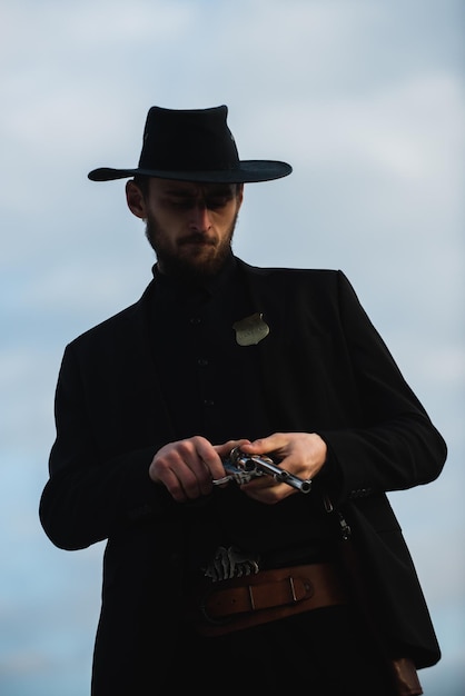 Tireur de cow-boy en costume noir et chapeau de cow-boy Homme sérieux avec des fusils de l'ouest sauvage revolver pistolet rétro et munitions de maréchal American western Sheriff Wild west voulait concept