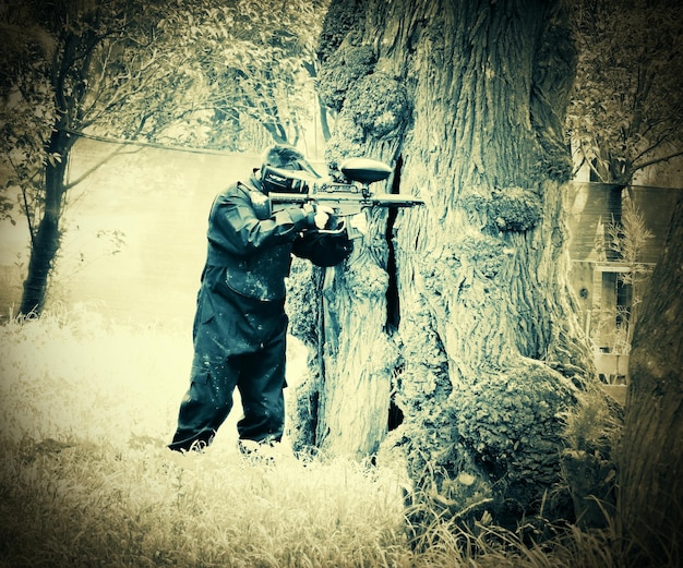 Photo le tireur de paintball se cache derrière un arbre.