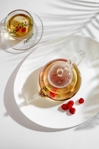 Tisane de baies rouges au thym et framboise fraîche dans une théière en verre. Fond blanc avec fond