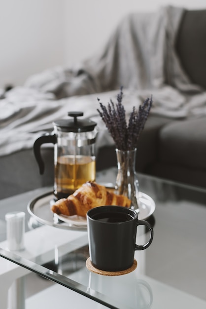 Tisane dans une tasse noire croissant et théière servie sur un plateau en métal avec bouquet de lavande séchée