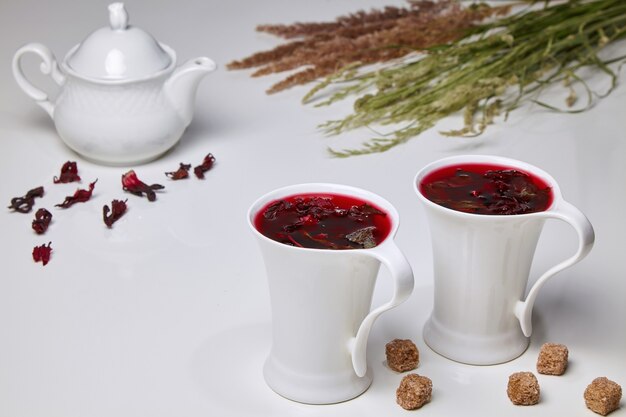 Tisane d'hibiscus à base de fleurs de rose et de menthe du Soudan avec des pinces à sucre de canne dans d'élégantes tasses blanches