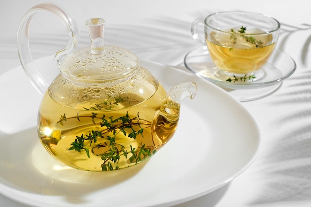 Tisane jaune au thym dans une théière en verre. Fond blanc avec fond.