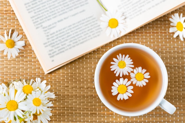 Tisane en porcelaine tasse à thé fleurs de camomille et livre sur tapis de rotin