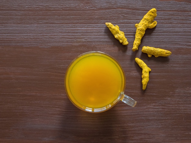 Tisane avec poudre de curcuma et racines de curcuma sur une table brune