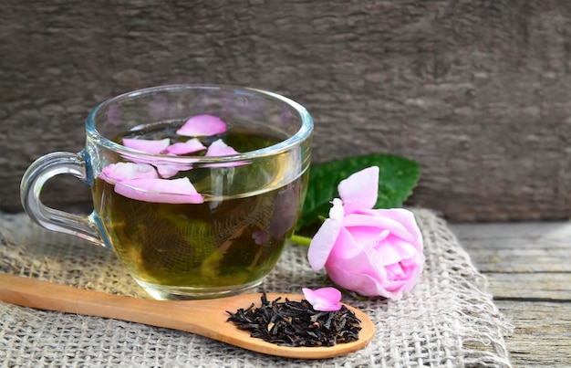 Tisane de rose dans une tasse en verre avec des pétales roses et des fleurs fraîches sur une table en bois rustique