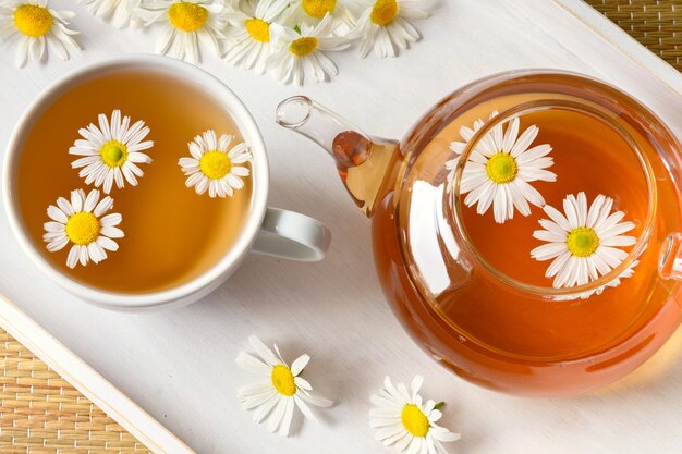 Tisane en tasse de fleurs de camomille et théière sur plateau en bois blanc