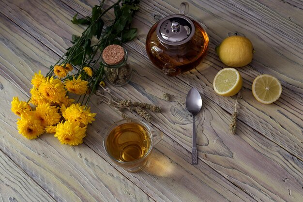 Tisane utile avec une plante Sideritis scardica ou thé de montagne grec avec du citron dans une tasse et des chrysanthèmes jaunes sur une table en bois en gros plan