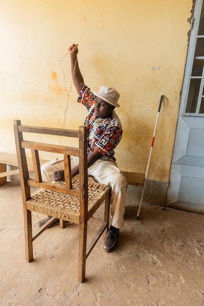 Tisser le siège d'une chaise en bois par un homme aveugle africain Concept d'artisanat de la cécité