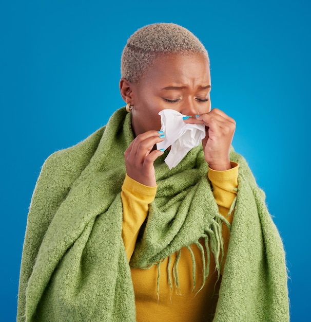 Photo tissu de femme noire malade et se moucher en studio fond bleu ou allergies au rhume des foins virus du froid ou de l'hiver modèle féminin éternuement et allergie à la grippe de problème de santé risque covid ou sinusite