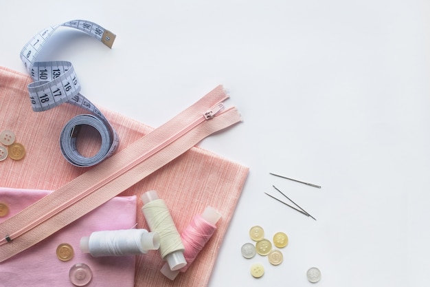 Photo tissu rose, fils à coudre, fermeture à glissière, aiguille, boutons et centimètre à coudre. vue de dessus, flatlay