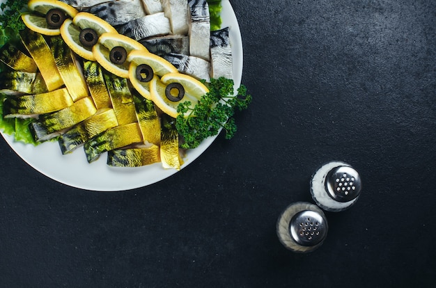 Sur des tissus sombres, dans l'assiette se trouve un beau poisson, hareng, et saumon agrémenté de verdure