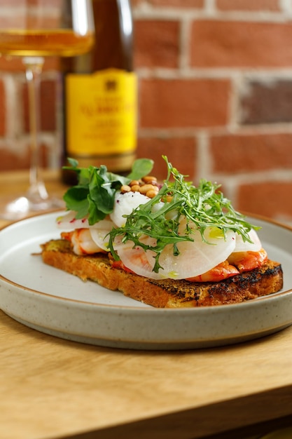 Toast aux crevettes grillées et légumes oeuf poché et herbes sur le dessus servi au restaurant Bouteille de vin et verre sur fond