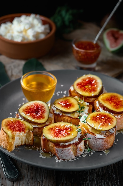 Toast aux fruits sur baguette grillée aux figues et fromage de chèvre sur une assiette avec du miel, graines de sésame