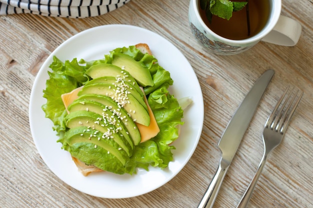 Toast à L'avocat Sur Pain De Blé Avec Salade De Fromage Et Graines De Sésame Sur Une Plaque Blanche Sur Une Table En Bois