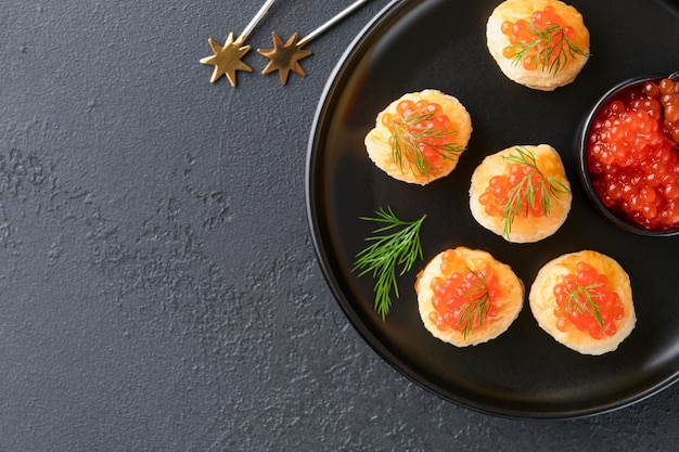 Toast de caviar rouge de saumon canapé de Noël ou toast avec du caviar rouge sur une assiette noire sur fond sombre Idée pour une collation de Noël Nourriture gourmande Texture du caviar Fruits de mer