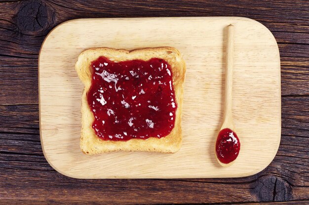 Toast avec confiture et cuillère sur une planche à découper. Vue de dessus