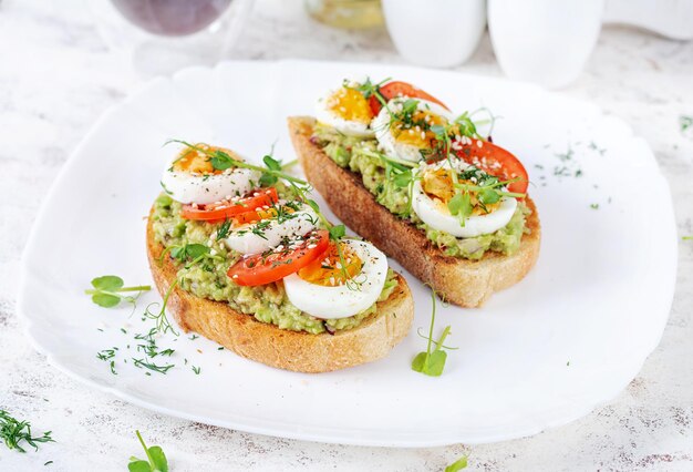 Photo un toast délicieux avec de l'avocat, des tomates, des œufs bouillis et du microgreen sur une assiette blanche.