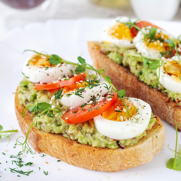 Photo un toast délicieux avec de l'avocat, des tomates, des œufs bouillis et du microgreen sur une assiette blanche.