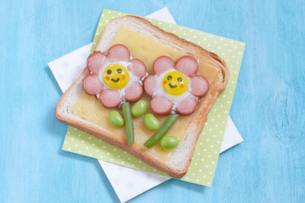 Toast drôle avec du fromage et des fleurs faites de saucisses, haricots verts et œufs de caille