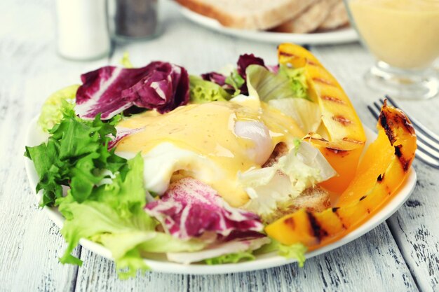 Toast avec oeuf Benedict et verts sur plaque sur table en bois