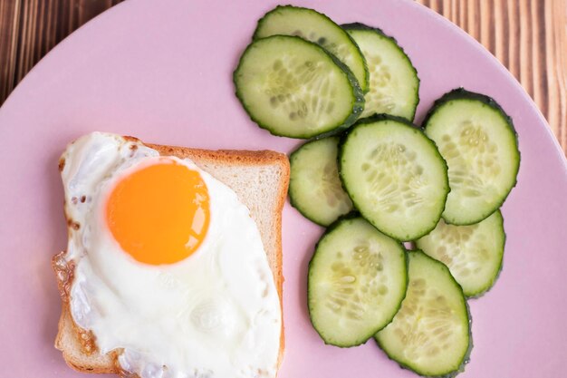 Photo un toast avec des œufs sur une assiette des concombres frais une tranche de pain blanc