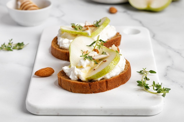 Toast de pain avec fromage à la crème fromage ricotta miel poire thym sur tableau blanc et table en marbre Snack bruschetta Close up