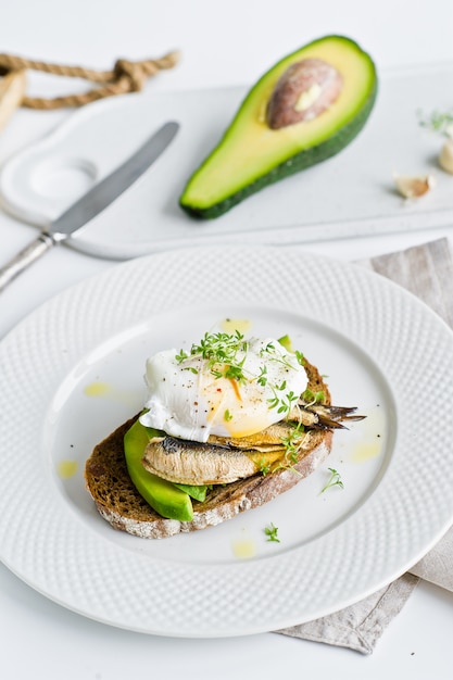 Toast de pain noir avec avocat, oeuf poché et sprats.