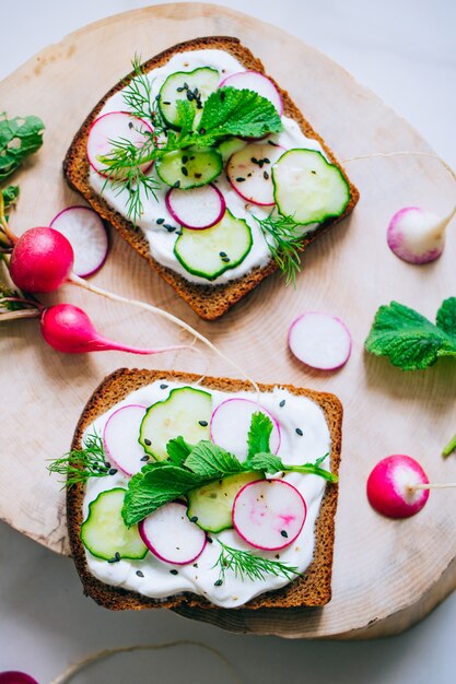 Toast avec radis, concombre et sésame noir de pain noir sur un fond de marbre clair