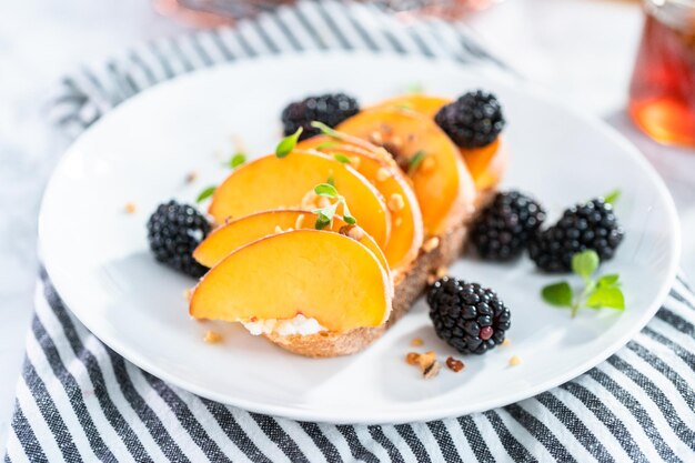 Toast de ricotta aux pêches garni de mûres sur une assiette blanche.