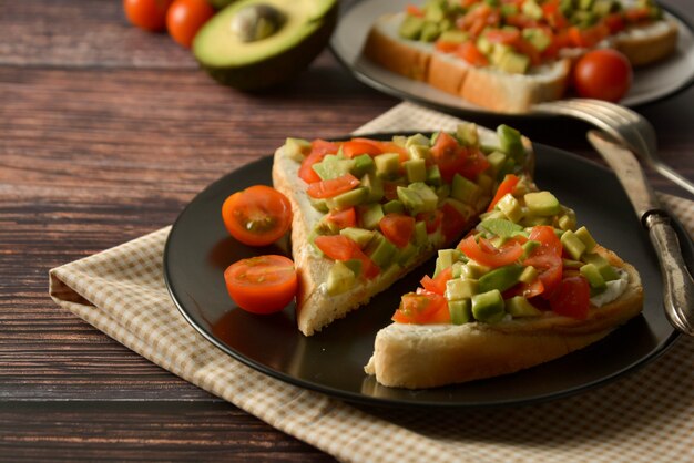 Toast sain avec avocat, tomates cerises et fromage sur une assiette. Table en bois.