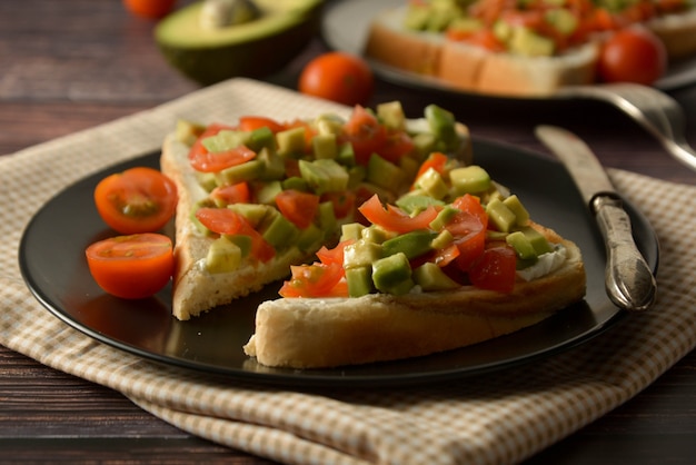 Toast sain avec avocat, tomates cerises et fromage sur une assiette. Table en bois.