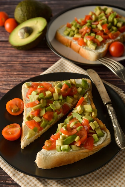 Toast sain avec avocat, tomates cerises et fromage sur une assiette. Table en bois.