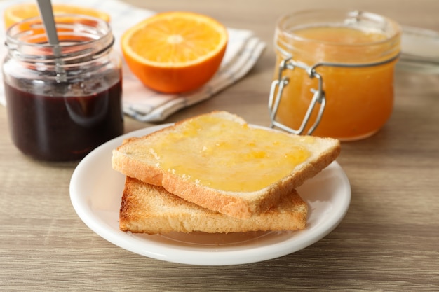 Toasts sur assiette, confiture, serviette et orange sur fond de bois, Close up