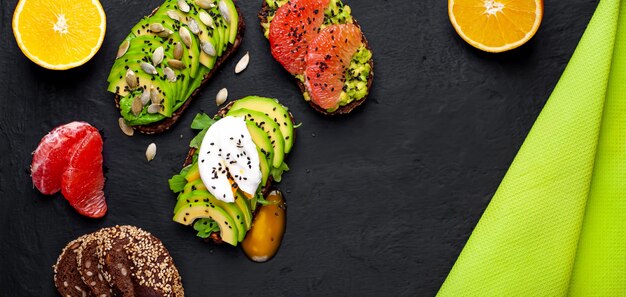 toasts à l'avocat, graines de sésame, pamplemousse, orange, œuf et café sur un fond noir en béton. délicieux petit déjeuner avec café et toasts