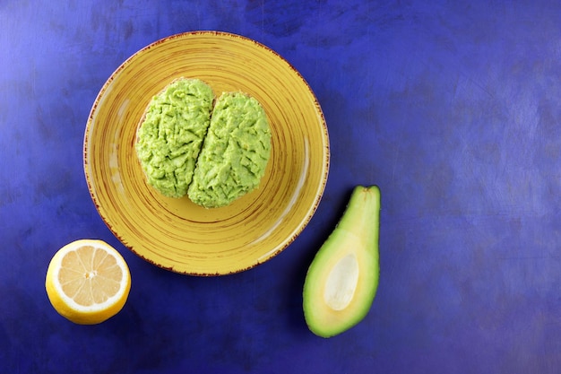 Toasts et avocat vert et citron jaune sur fond bleu Petit-déjeuner sain toasts avec avocat smash sur une plaque jaune Concept de cuisine végétarienne Gros plan